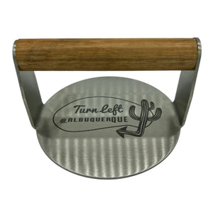Stainless burger smasher with Turn Left at Albuquerque logo and wooden handle